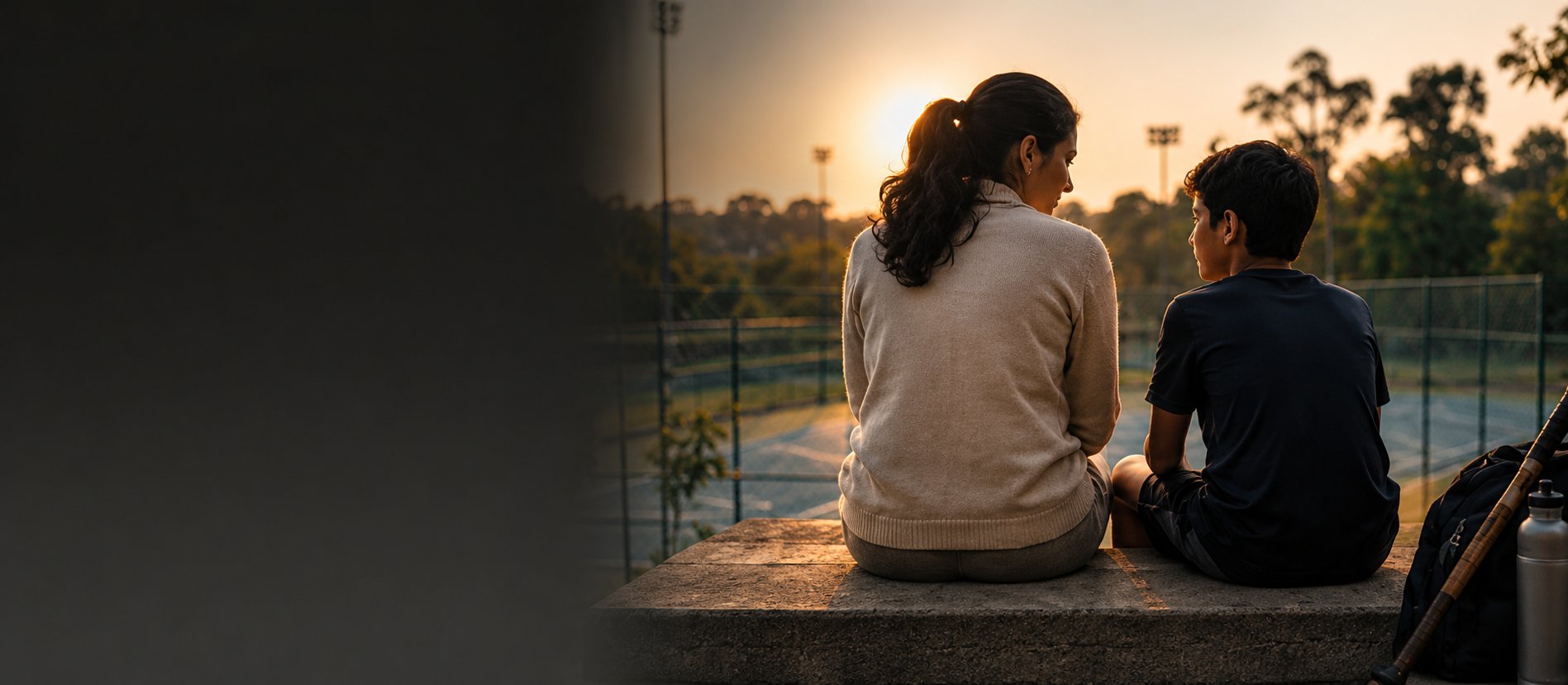 A mother and son sitting together on a courtside bench at sunset